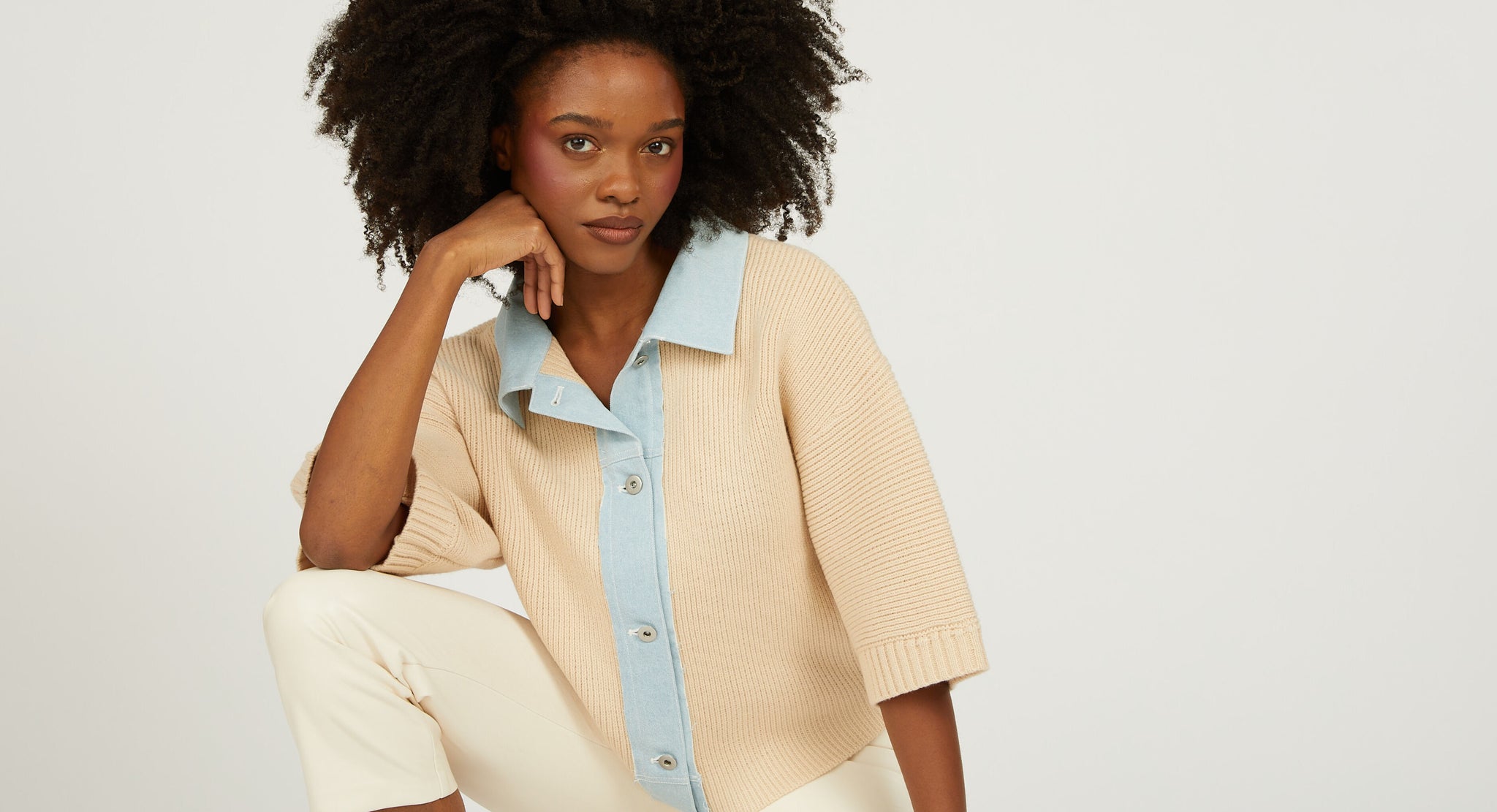 Woman wearing a beige sweater over a light blue shirt with a white background