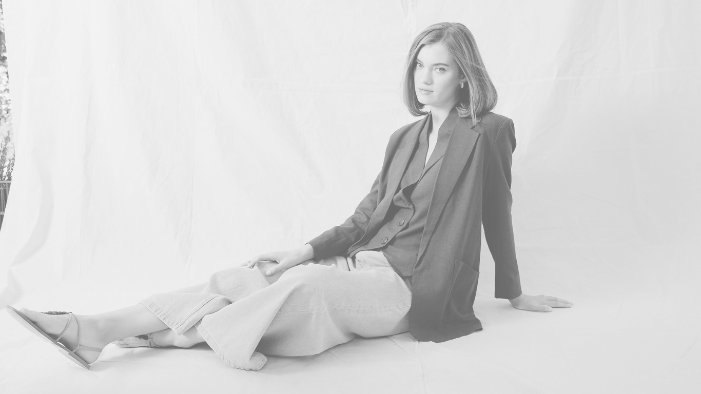 Person sitting on a white surface with a white curtain in the background
